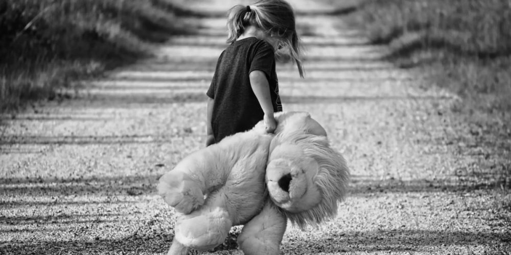 Black & White picture of child walking down road with stuffed toy