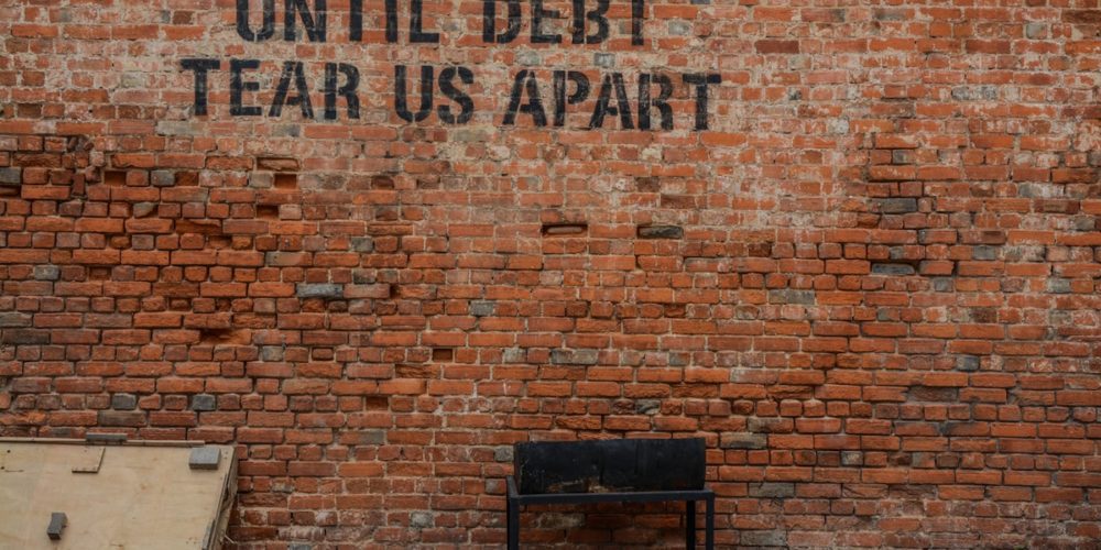 Until debt tear us apart written on a brick wall